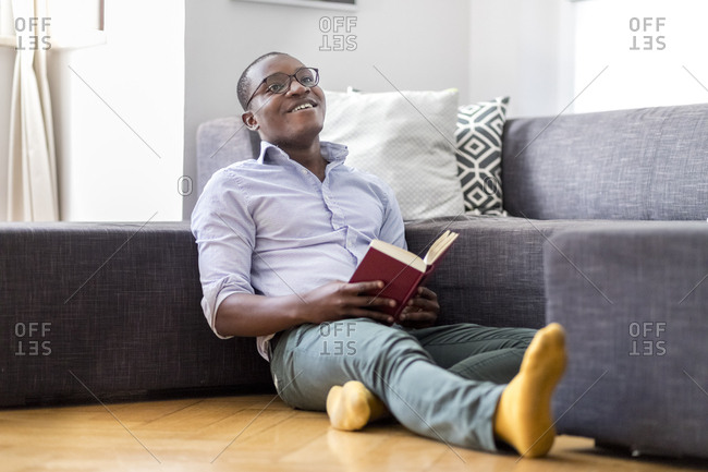 Happy young man sitting on the floor in the living room reading book