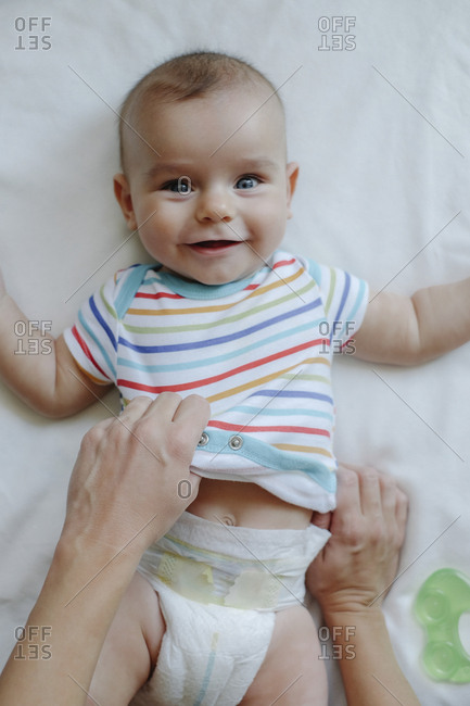 Portrait of smiling baby boy getting dressed by his mother