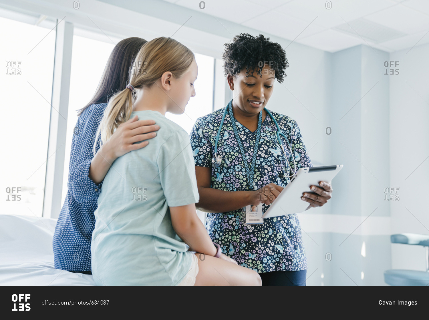 Pediatrician showing tablet computer to mother and daughter in medical examination room