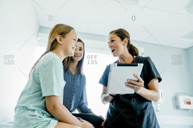 Low angle view of surprised pediatrician holding tablet computer while looking at girl sitting by mother in medical examination room