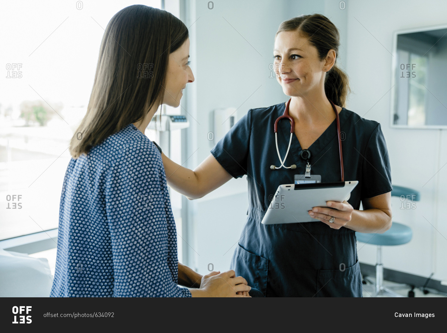 Female doctor consoling woman while holding tablet computer in medical examination room