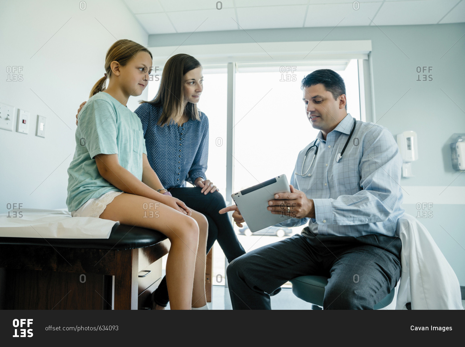 Pediatrician discussing over tablet computer with mother and daughter in medical examination room