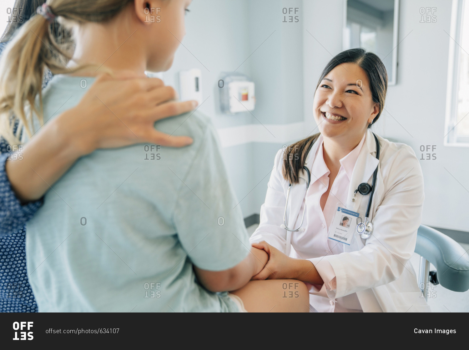 Cheerful pediatrician holding girl's hand sitting by mother in medical examination room