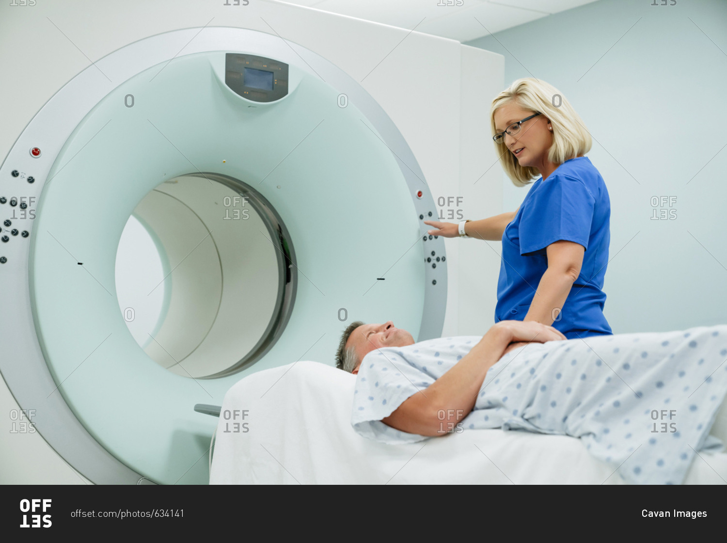 Nurse looking at patient lying on MRI Scanner while pressing start button in examination room