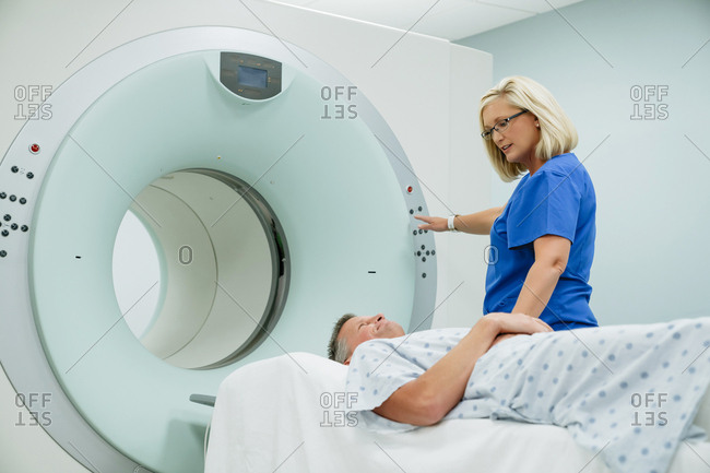 Nurse looking at patient lying on MRI Scanner while pressing start button in examination room