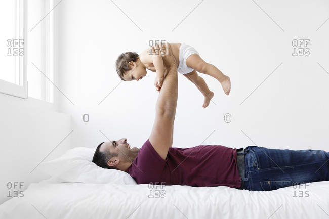 Cheerful father lifting shirtless daughter against wall at home