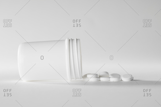 White medicine container with white pills on a white background