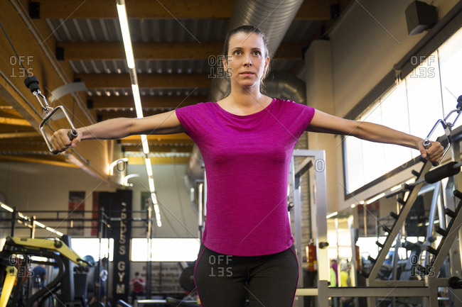 Concentrated sportswoman doing chest cable flys in machine