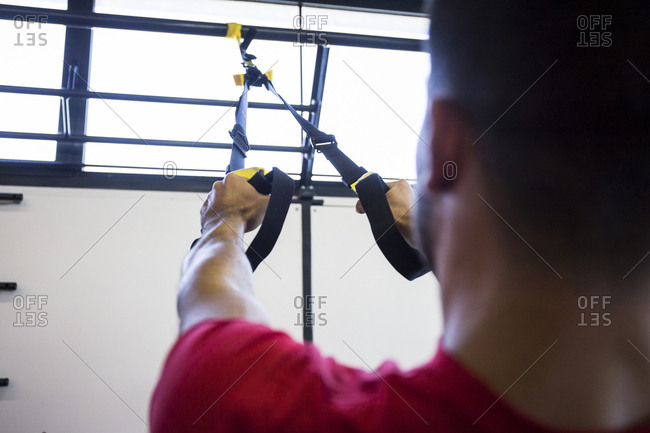 Sportsman doing suspension training in gym using special ropes