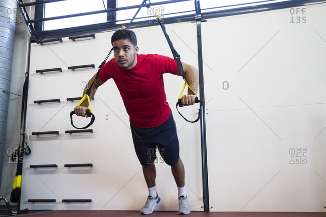 Concentrated sportsman doing suspension training hanging on straps and looking forward