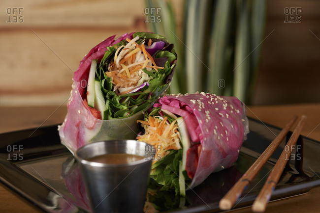 A vegan wrap served in soft rice paper including spinach, carrots, basil leaves, cabbage and served with sweet peanut sauce