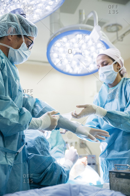 Female assistant helping doctor to get dressed before operation in surgery