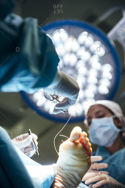 From below shot of surgeons stitching foot of patient in bright lamp light