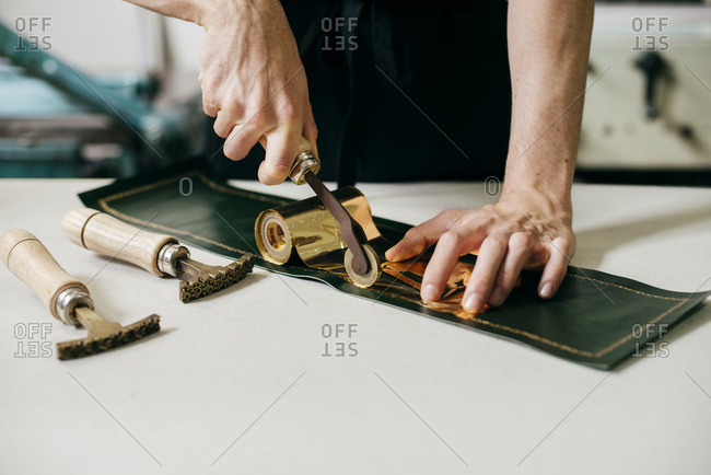 Crop shot of workman using tools and gold material while imprinting on leather