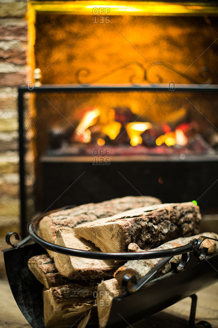 Stack of firewood composed near fireplace with burning flame at home