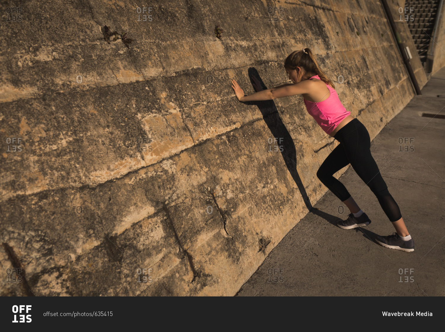 Female doing push-ups while standing near wall during sunset