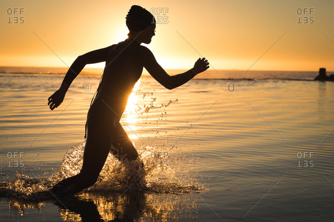 Woman in wetsuit running in water during sunset