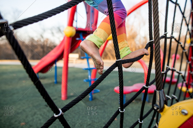 Child with dirty feet climbing rope structure at playground