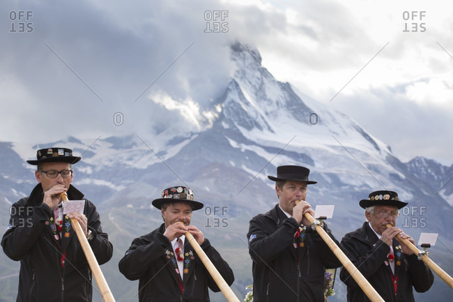 Zermatt, Wallis, Switzerland - August 25, 2014: Four traditionally dressed locals of Zermatt play the Alphorn in front of the Matterhorn mountain. With the passing of time, the alphorn almost totally disappeared as an instrument used by Swiss shepherds. It was only with the romanticism of the 19th century and the revival of folklore and tourism that the alphorn experienced a renaissance and even became a national symbol