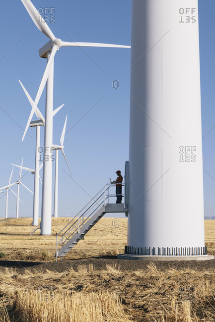 A wind farm technician standing and using a laptop at the base of a turbine on a wind farm in open countryside at Palouse.