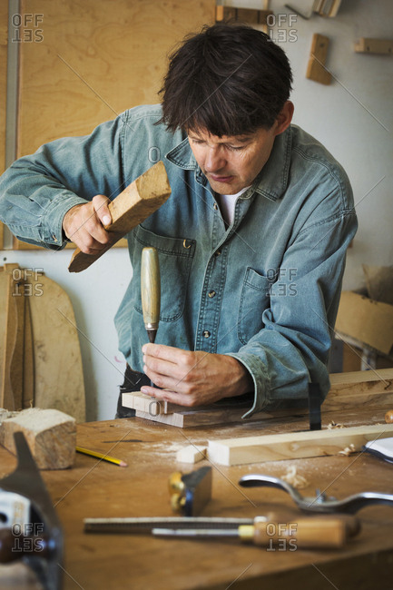 A craftsman using a piece of wood on the end of a chisel to mark a piece of wood.