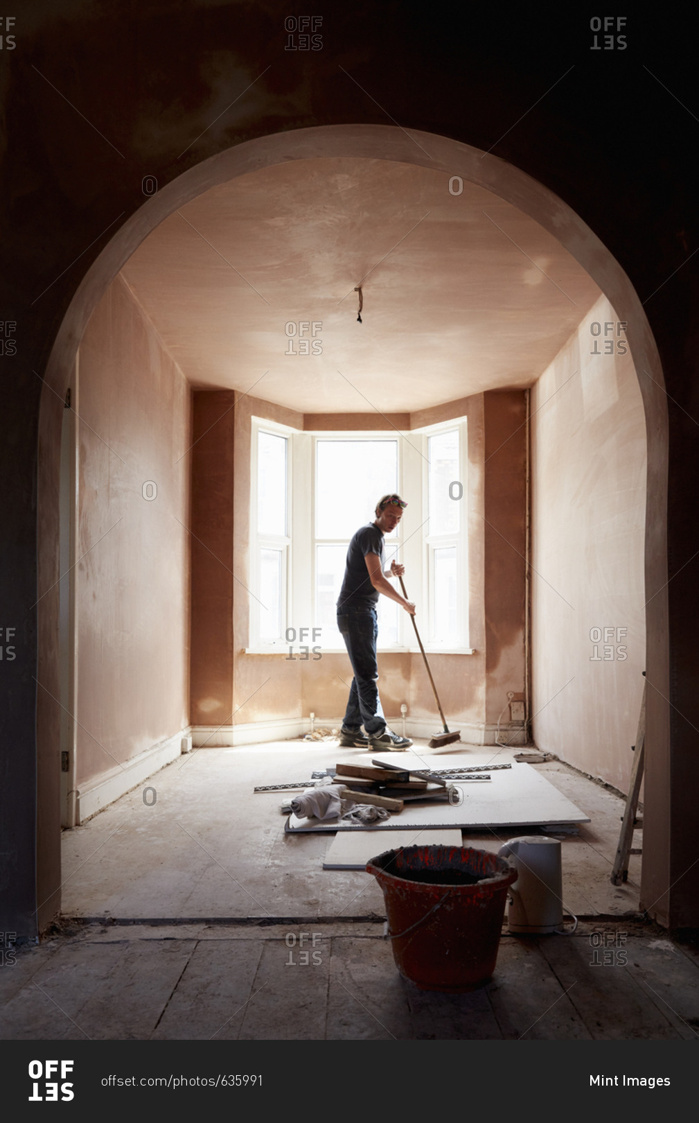 A builder sweeping and tidying up in a renovated replastered house with an archway.
