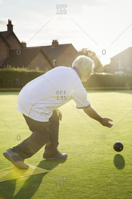 A lawn bowls player standing on a small yellow mat preparing to deliver a bowl down the green, the smooth grass playing surface.