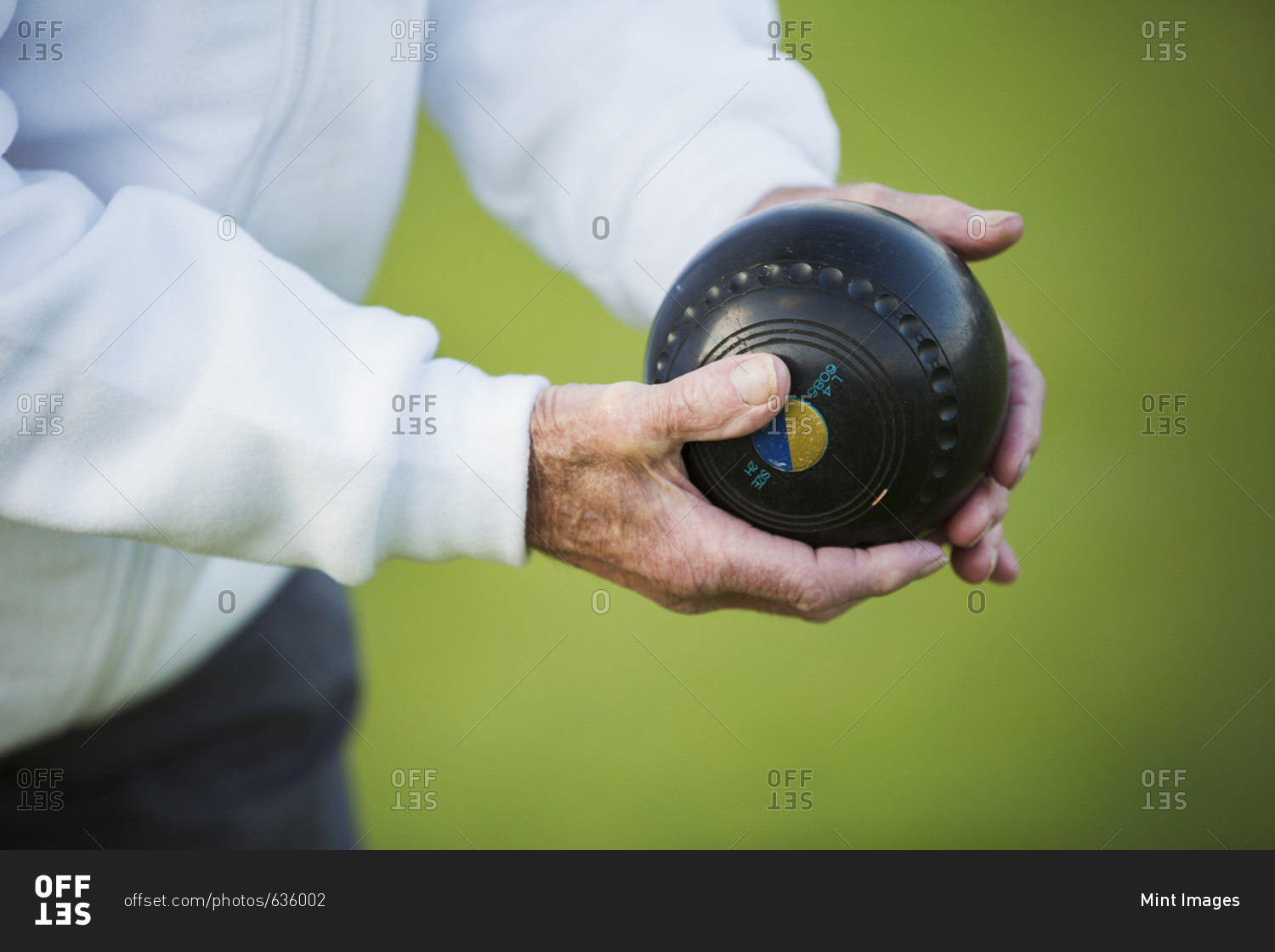 A man holding a black wooden lawn bowls ball in his hands. Notches and