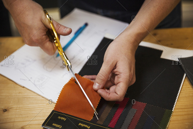A person using shears to cut a fabric sample at a workbench, overhead view.