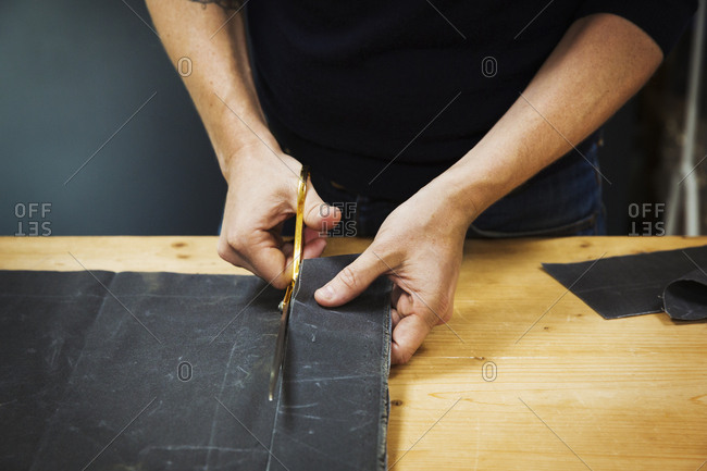 A man cutting a piece of grey fabric with shears.