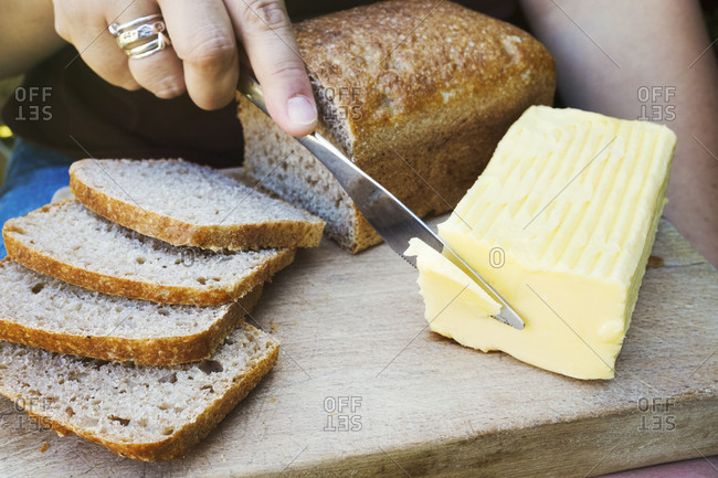 A person with a knife slicing through a block of butter for a sliced bread loaf.