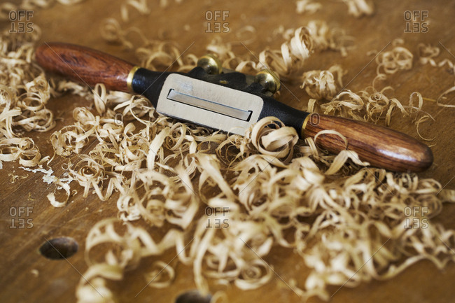 A traditional spokeshave with smooth wooden handles on wood covered with fresh curled wood shavings.