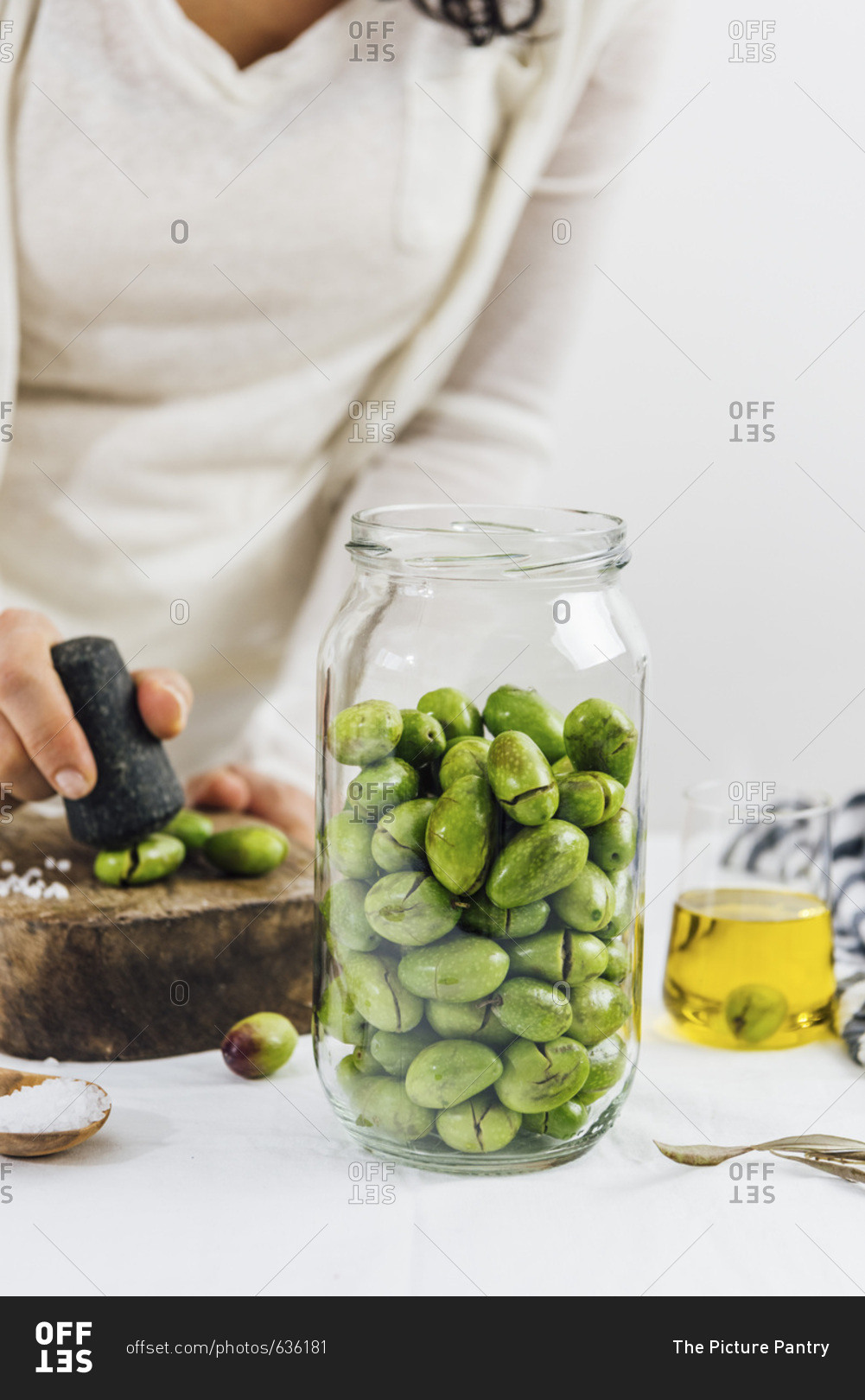A woman cracking olives for brining a glass jar full of green olives