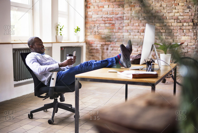 Businessman sitting in office with feet up on desk - Stock Photo