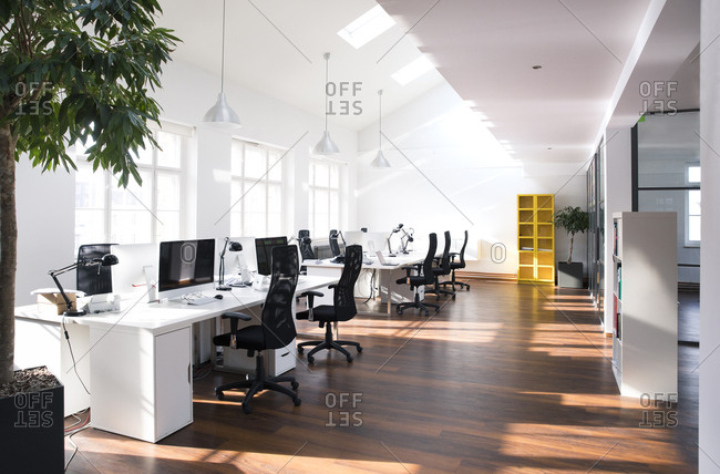 Desks with PCs in bright and modern open space office stock photo - OFFSET