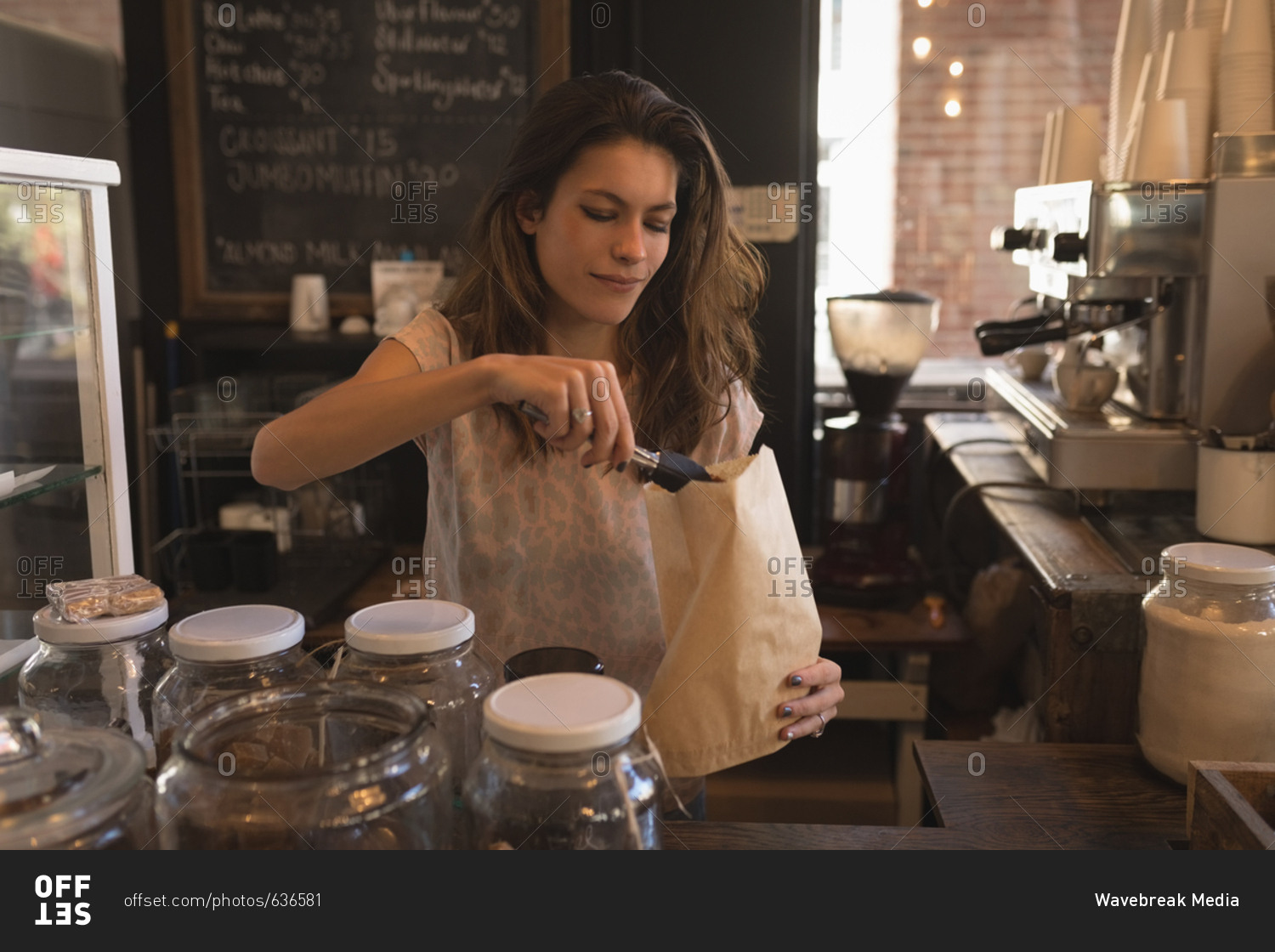 Waitress packing sweet food in paper bag at counter in coffee shop