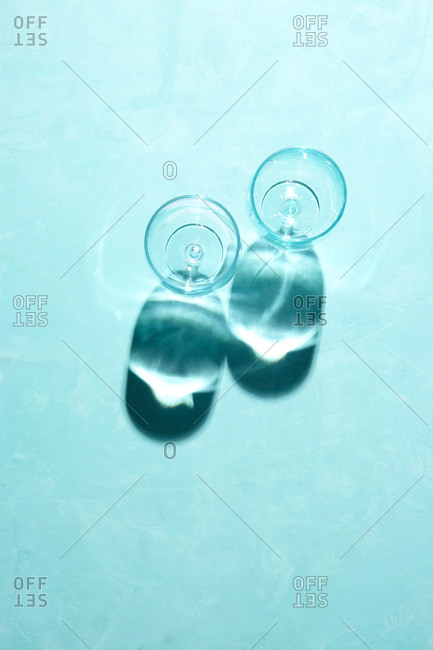 Two glass cups with harsh shadows on a solid bright blue background