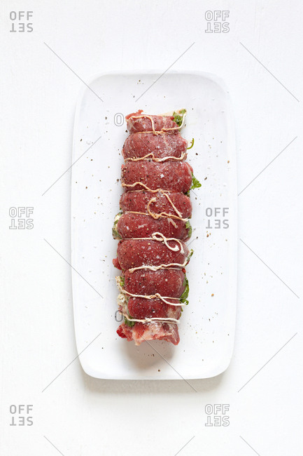 Overhead raw steak roll up raw on white plate isolated against white background