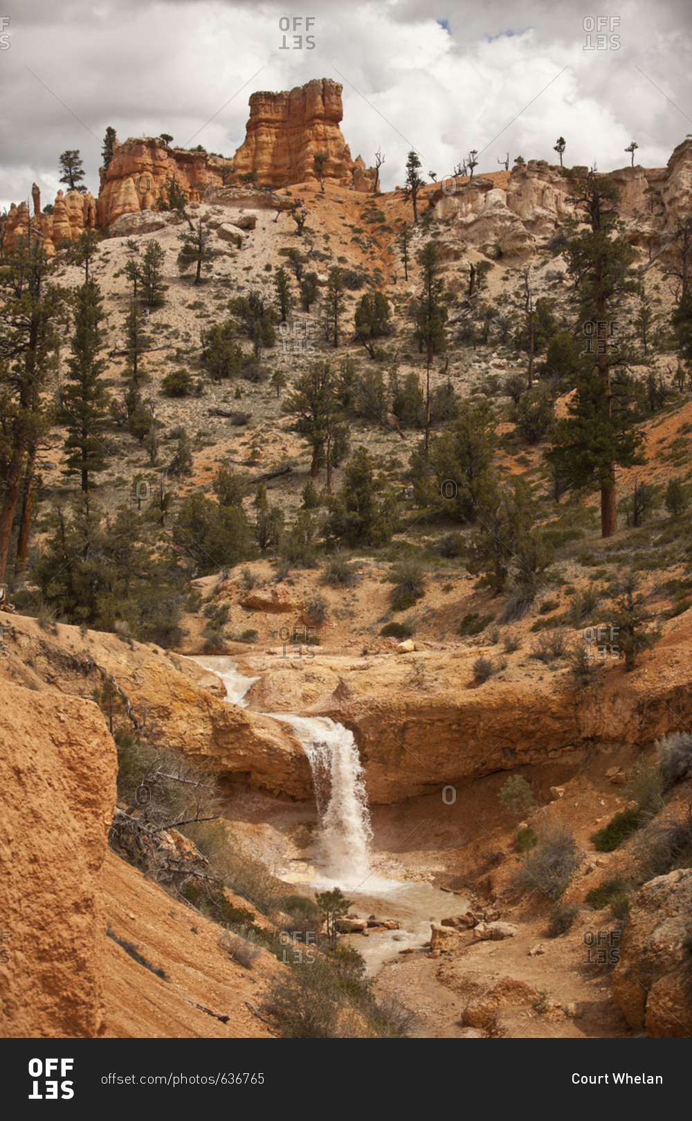 Waterfall at the base of an arid mountainside topped by rock formations