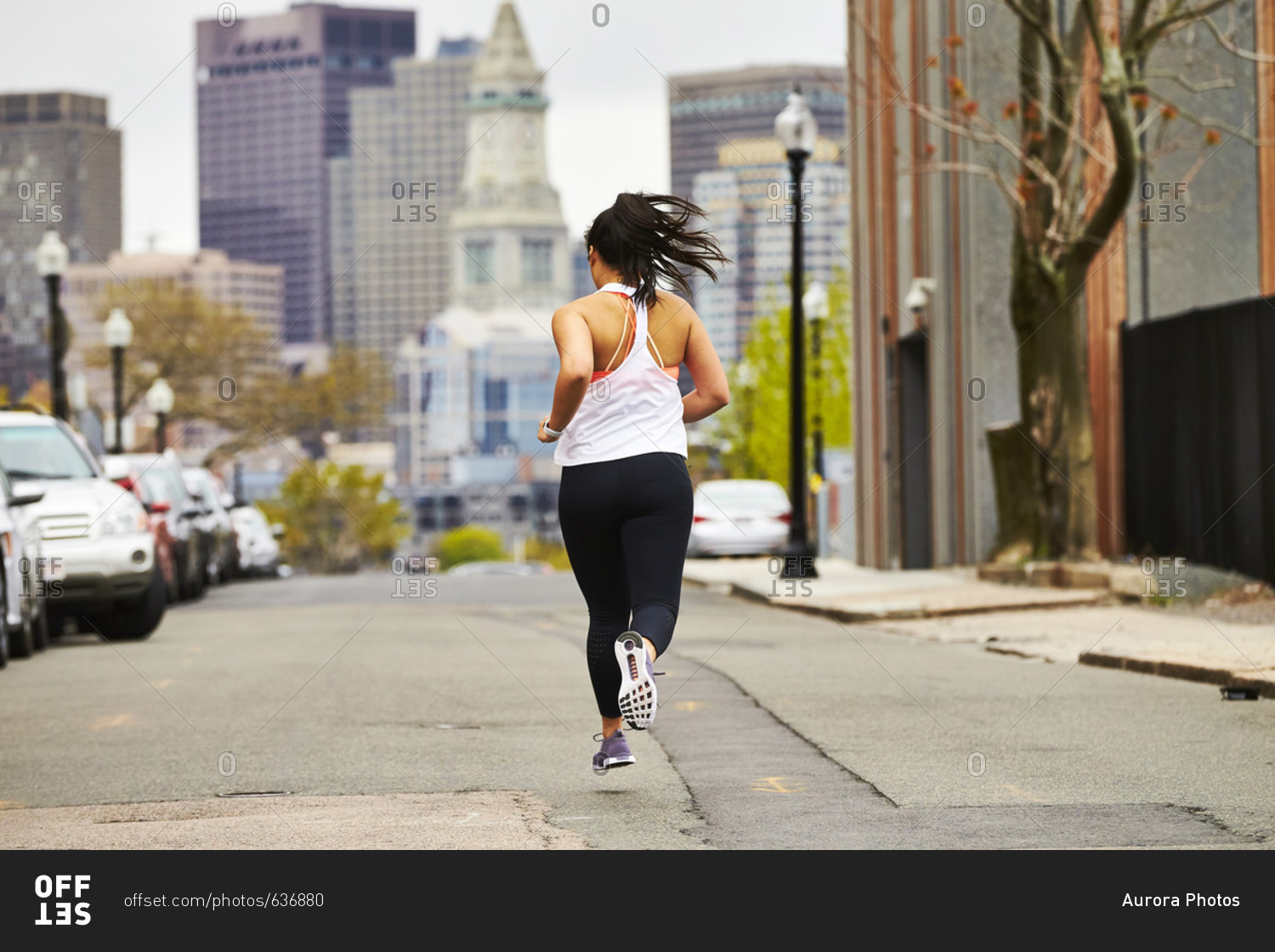 A female runner running towards the Boston skyline.