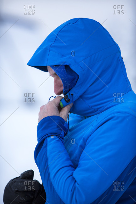 Side view of backcountry skier adjusting hood of blue jacket, Clinton, Montana, USA