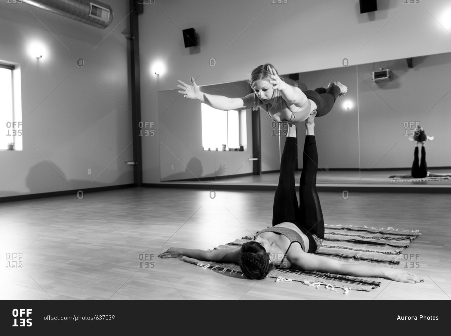 Two fit females practice acro yoga together inside a yoga studio