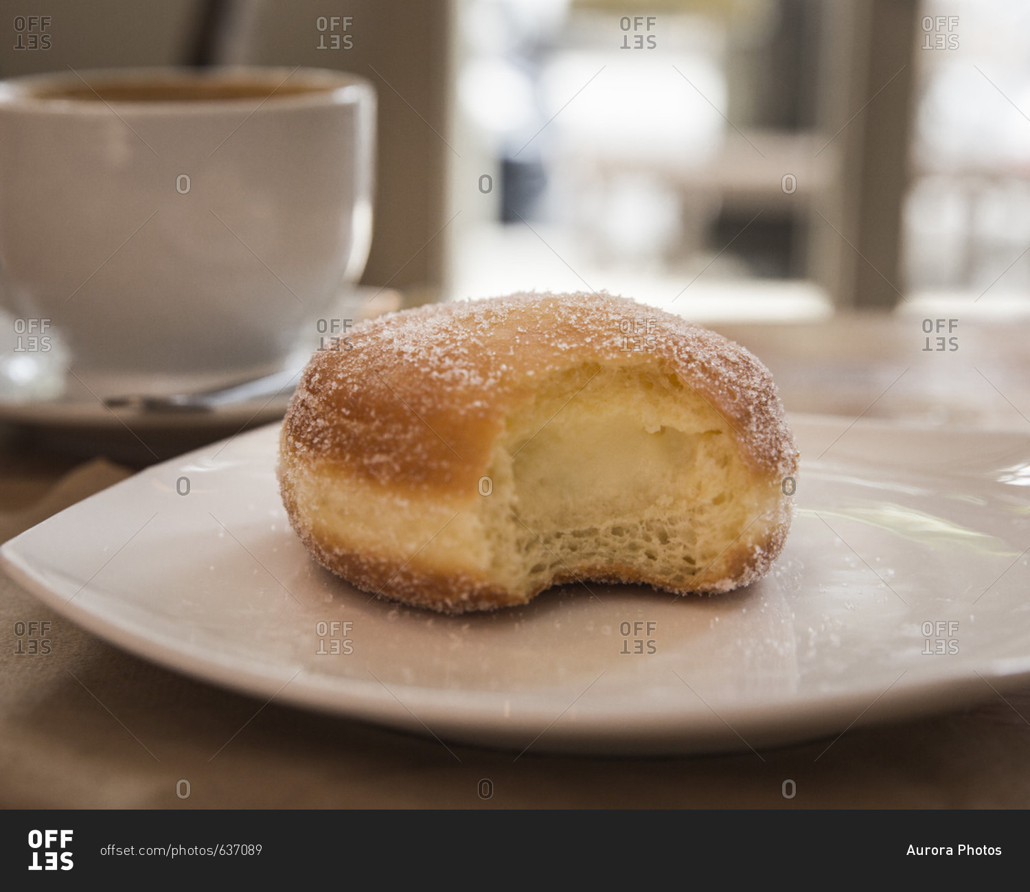 Vanilla cream doughnut with missing bite on white plate and coffee in background, Brooklyn, New York City, USA