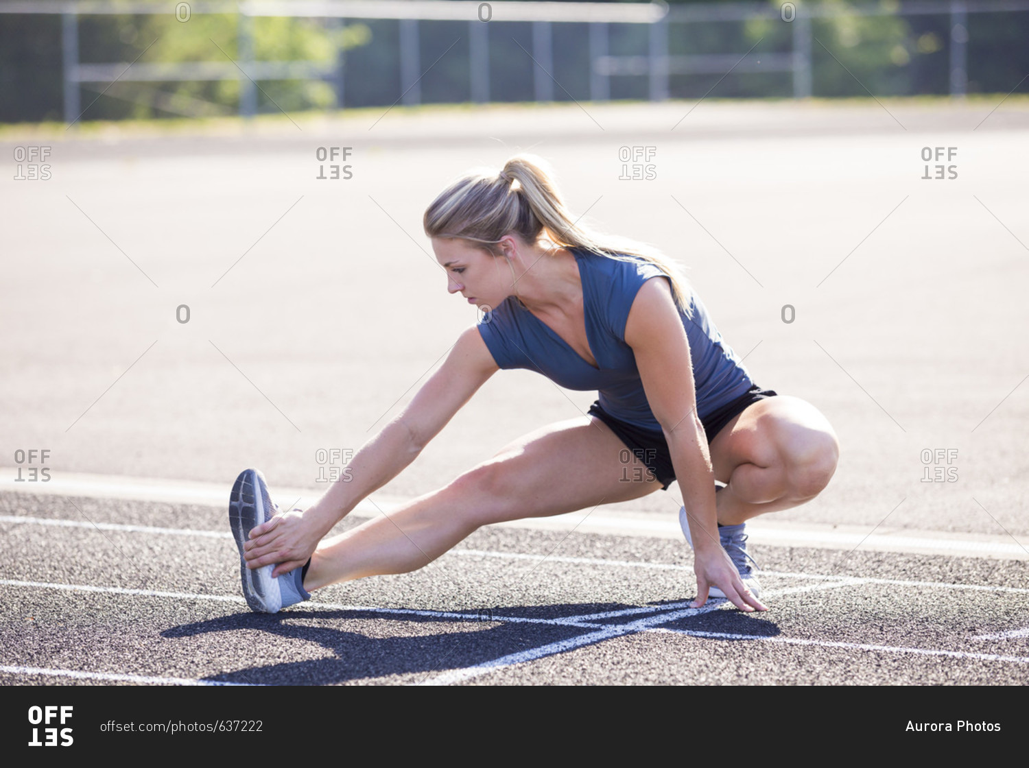 Female runner with blonde hair and ponytail stretching before running on track, Eugene, Oregon, USA