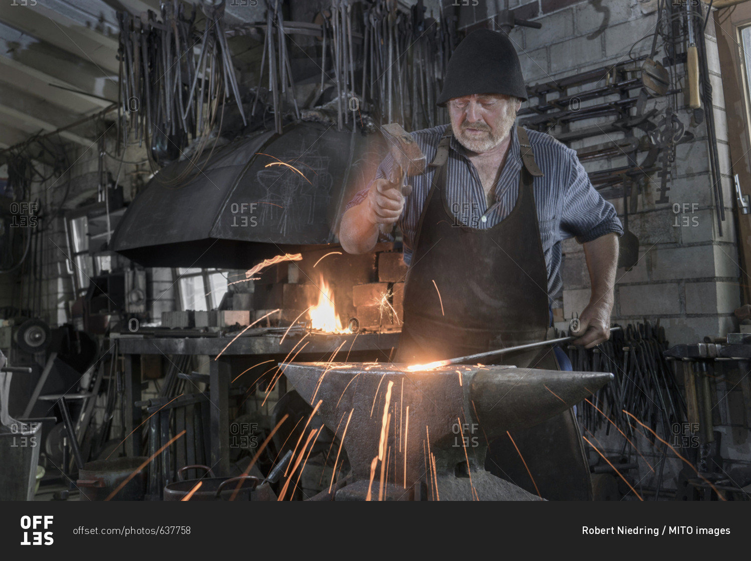 Blacksmith hammering hot iron bar on anvil at workshop