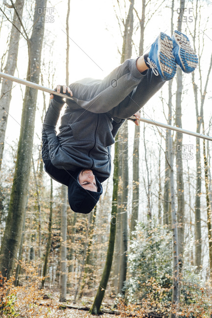 Low angle view of man hanging upside down on pole in forest against sky