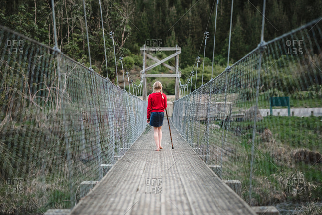 Little girl walking on bridge with a walking stick