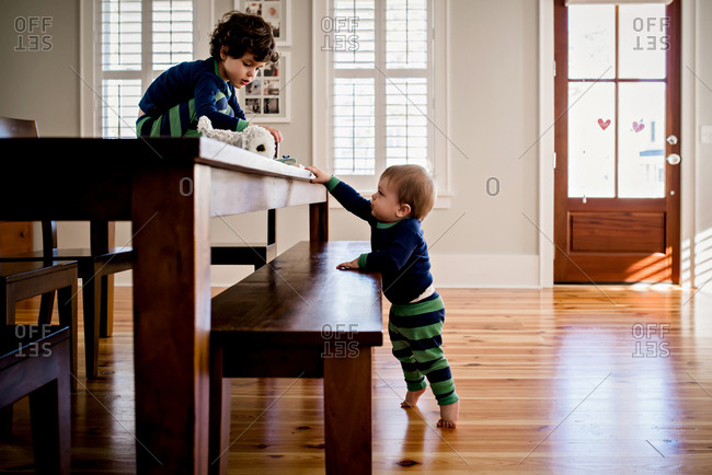 Boy sitting on table as baby brother reaches up to him