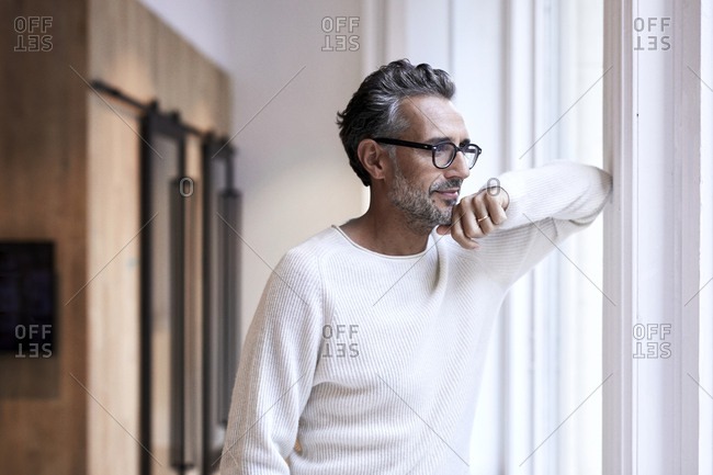 Thoughtful mature businessman standing by window at creative office