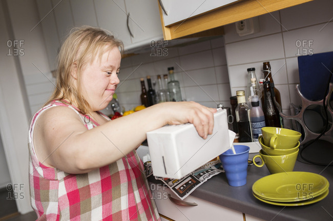 Woman with Down syndrome pouring milk to mug in kitchen